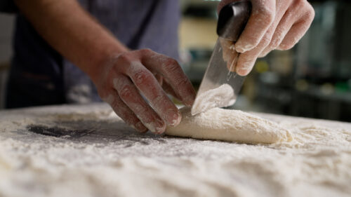 Baker dividing dough with bench scraper on floured surface.